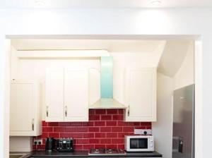 a kitchen with white cabinets and a red brick wall at Excel House Serviced Apartments in Leeds