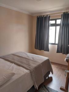 1 dormitorio con 1 cama y una ventana con cortinas en Apartamento Conforto, en Curitiba