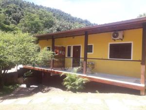 a yellow house with a porch and a mountain at Chalés Azuleto - Ilhabela in Ilhabela