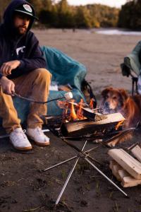 a man and a dog sitting next to a campfire at Ocean Village Resort in Tofino