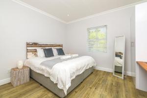 1 dormitorio blanco con 1 cama grande y espejo en Irene Avenue Apartment - With backup Electricity!, en Somerset West