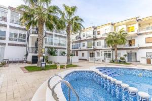 a swimming pool in front of a building with palm trees at Punta Prima Palm Beach Apartment in Punta Prima