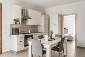 - une cuisine avec des placards blancs, une table et des chaises dans l'établissement Delia case vacanza, à Fiumefreddo di Sicilia