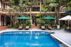 a swimming pool with chairs and umbrellas next to a building at Saem Siemreap Hotel in Siem Reap