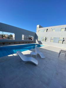 a swimming pool with two white chairs next to a building at Hotel Torrevado in Las Grutas +48 photos