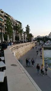 a group of people walking down a sidewalk near the water at Piraeus historical center in Piraeus