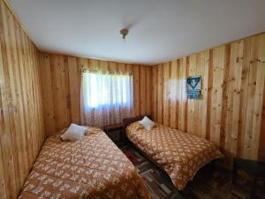 two beds in a room with wooden walls at Cabaña Nuevo Amanecer in San José de la Mariquina