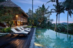 a pool with lounge chairs next to a building at Villa Inka Ubud by Nakula in Ubud