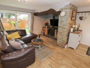 a living room with a leather couch and a stone fireplace at Bwthyn Y Jacdo in Whitechurch