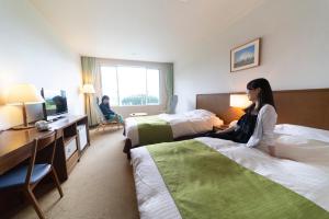 una mujer sentada en una cama en una habitación de hotel en Kyukamura Fuji en Fujinomiya