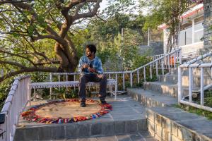 un hombre sentado en un banco bajo un árbol en StayVista at Meraki Homestay - 2BR Pet Friendly Villa in Dharamshala, en Dharamshala