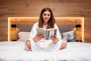 a woman sitting on a bed reading a book at Weber Hofmark Apartments in Bad Birnbach