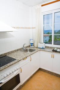cocina con armarios blancos, fregadero y ventana en Aparthotel Cabicastro en Portonovo