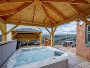 uma banheira de hidromassagem num pátio com telhado de madeira em Westertonhill Lodge 8 Newbuild with Hot Tub Option em Balloch