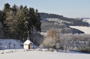 eine kleine Kapelle auf einem schneebedeckten Feld mit Kreuz in der Unterkunft Wüllner's Landgasthof in Schmallenberg