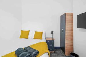 1 dormitorio con 1 cama con almohadas amarillas y TV de pantalla plana en Modern Equipped 4 BR House in Central Stoke-Free Parking en Stoke on Trent