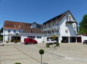 ein großes weißes Gebäude mit einem roten Van auf einem Parkplatz in der Unterkunft Hotel Hellers Twenty Four II -24h-Check-In- in Friedrichshafen