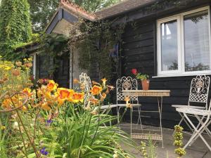 New Listing - Idyllic cottage in a beautiful Kent setting في Kent: كوخ أسود فيه ورد وطاولة وكراسي