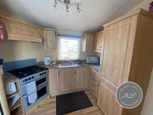 eine Küche mit Holzschränken und einem Herd mit Backofen in der Unterkunft Coral Beach - Row 73 Van 2, central heating, WiFi, bed linen - Meadow Lakes Caravan & Lodge Hire in Ingoldmells + 7 Fotos