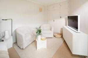 a white bedroom with a white chair and a tv at Haus Sandy Wohnung 4 in Norderney