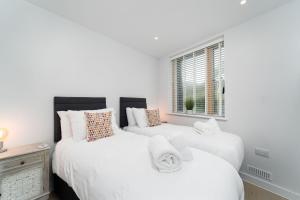two beds in a bedroom with white walls and a window at Surfside in Hayle