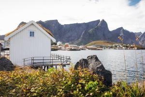 a white building next to a body of water with mountains at Toppøy Rorbuer in Reine
