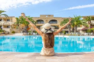 a woman sitting next to a swimming pool with her arms up at Hotel Costa dei Fiori in Santa Margherita di Pula