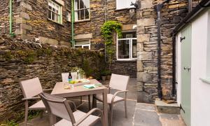 a patio with a table and chairs and a stone wall at Hazel Cottage in Ambleside