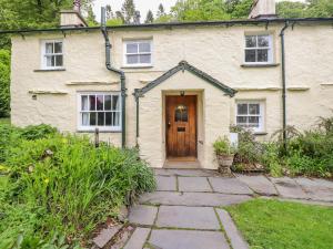 a white house with a wooden door in a yard at Fir Tree Cottage in Ambleside