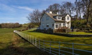 a white house on a green field with a fence at Juniper Cottage in Windermere