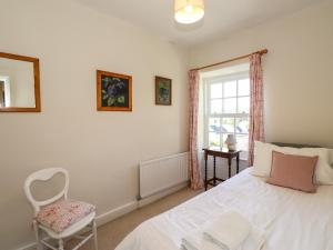 a bedroom with a white bed and a chair and a window at Jessicas Cottage in Bowness-on-Windermere