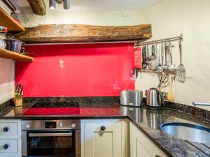 cocina con pared roja y fregadero en Knotts Cottage, en Windermere