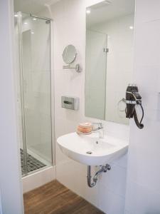 La salle de bains blanche est pourvue d'un lavabo et d'une douche. dans l'établissement Tante ALMA's Mülheimer Hotel, à Mülheim
