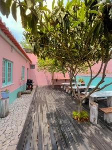a wooden deck with a tree and a pink building at Kali Vice Surf Villa in Costa da Caparica
