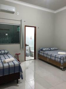 two beds in a white room with a bathroom at Casa dos Ventos Barreirinhas in Barreirinhas