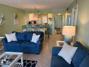 a living room with two blue couches and a kitchen at Sandcastles 704- Space Coast Oceanview! in Cocoa Beach