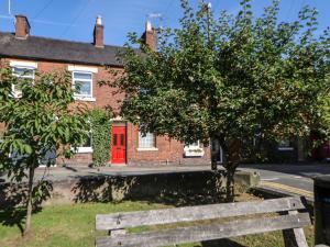 a wooden bench in front of a brick house with a red door at Mill Cottage in Leek