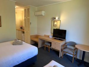 um quarto de hotel com uma cama e uma secretária com uma televisão em Banjo Paterson Motor Inn em Lakes Entrance