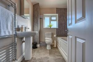 a bathroom with a sink and a toilet and a window at Stratton Heights by Apricity Property - 3 bedroom house, great for work or leisure, pet friendly in Cirencester