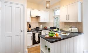 cocina con armarios blancos y encimera negra en Lingmell House, en Windermere