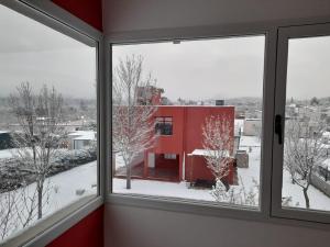 una ventana con vistas a un edificio rojo en la nieve en Posada Valle del Sol en Potrero de los Funes