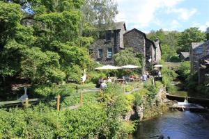 a group of people sitting under umbrellas next to a river at The Miller in Ambleside