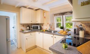 una cocina con armarios blancos y fregadero en Kent Cottage, en Cockermouth
