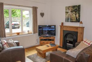 een woonkamer met een televisie en een open haard bij Four Seasons Cottage in Ambleside
