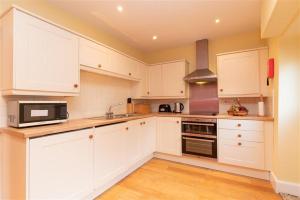 a white kitchen with white cabinets and a microwave at Millcroft Cottage in Penrith