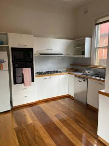 a kitchen with white cabinets and a wooden floor at Central CBD House in Wagga Wagga