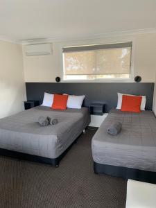 two beds in a room with two red pillows at Altona Motel in Uralla
