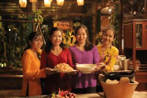 4 femmes debout dans une cuisine tenant une assiette de nourriture dans l'établissement Vamxang Rustic Home, à Cần Thơ