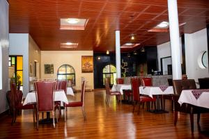 The Garden Place Hotel في روهينجيري: غرفة طعام مع طاولات بيضاء وكراسي حمراء