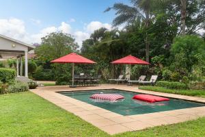 a swimming pool with two red umbrellas in a yard at Isoyi On The Mill in Durban